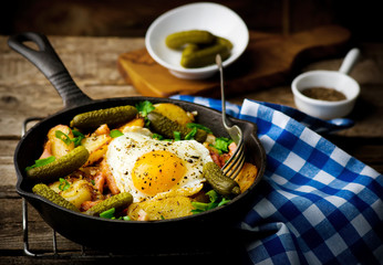 country breakfast from potatoes, with bacon and fried eggs in a pig-iron frying pan. style rustic. selective focus