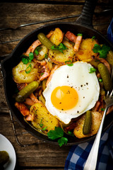 country breakfast from potatoes, with bacon and fried eggs in a pig-iron frying pan. style rustic. selective focus