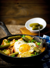 country breakfast from potatoes, with bacon and fried eggs in a pig-iron frying pan. style rustic. selective focus