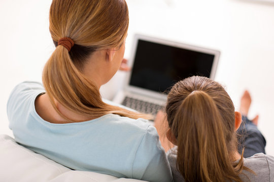 Rear View Of Mother And Little Daughter Using Laptop