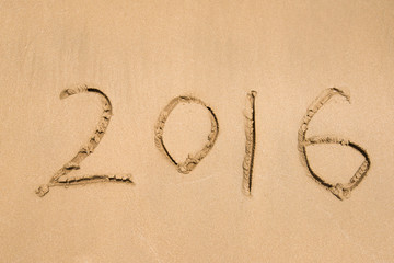 Year 2016 hand written on the white sand in front of the sea
