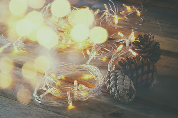 abstract double exposure photo of pine cones next to gold garland lights on wooden background. copy space. retro style filtered

