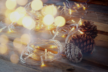 abstract double exposure photo of pine cones next to gold garland lights on wooden background. copy space. retro style filtered
