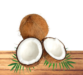 halfs of coconut on green leaves on wooden table over white