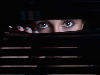 Young woman looking behind a blind