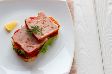 cheese sandwich with meat and vegetables on a white plate with a slice of lemon