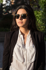 Businesswoman. Pretty Latina business woman posing in a photo session in the sun. She wears sunglasses and elegant black suit with white shirt. 