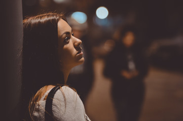Sad young lady thinking about something leaning against street lamp