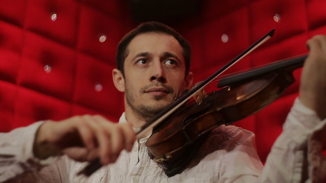 Elegant emotional man violinist fiddler playing violin in red background
