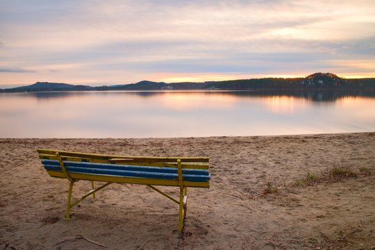 Colorful autumn evening. Empty wooden bench on beach of lake. © rdonar