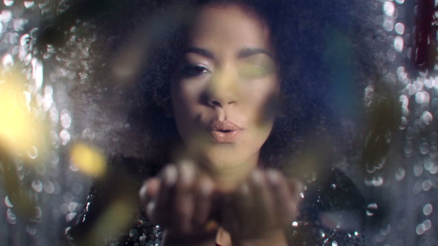 Beautiful afro american woman blowing gold glitter, slow motion.