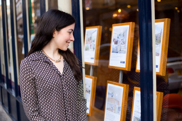 young woman looking in the window of an estate agent