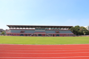 Red treadmill, track running at the stadium with green grass on blue sky