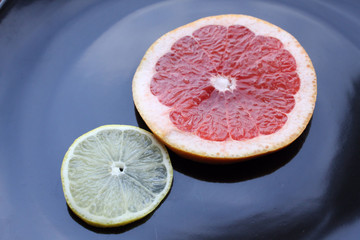 Sliced pieces of grapefruit and lemon on black glossy plate