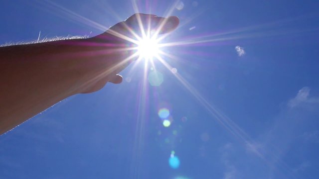 Hand to Bright Sun Against Blue Sky. Slow Motion.