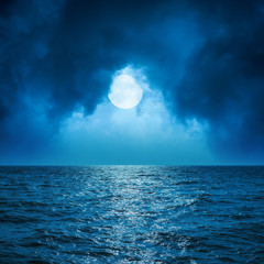 full moon in clouds over dark blue sea