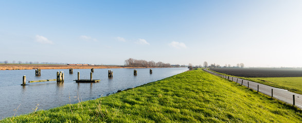 Grassy dike along a canal with wooden bollards