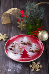 Homemade Christmas cookies in the shape of a Christmas tree, sprinkled with powdered sugar on a dark wooden table with festive decorations, selective focus