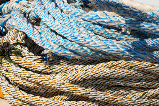 Close up of Weathered Nautical Ropes / Detail of weathered nautical ropes, white, blue, green and orange, on the pier in the harbor