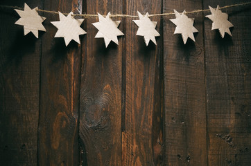 Simple Christmas cardboard stars garland decoration on dark wood background.