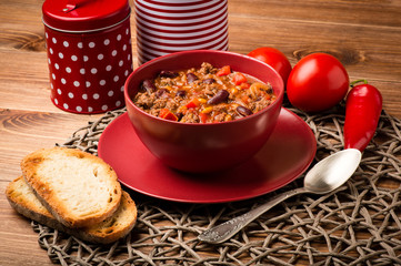 Chili con carne served in the red bowl on the wooden background.