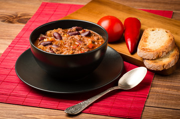 Chile con corne served in the black bowl on the wooden background.