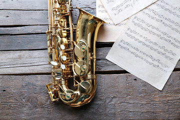 Beautiful golden saxophone with musical notes on wooden background, close up