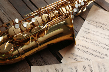 Naklejka premium Beautiful golden saxophone with musical notes on wooden background, close up