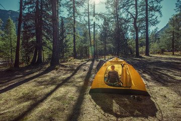 Woman hiker sitting in yellow tent in mountain woods in  lotus position relaxing and doing yoga exercise