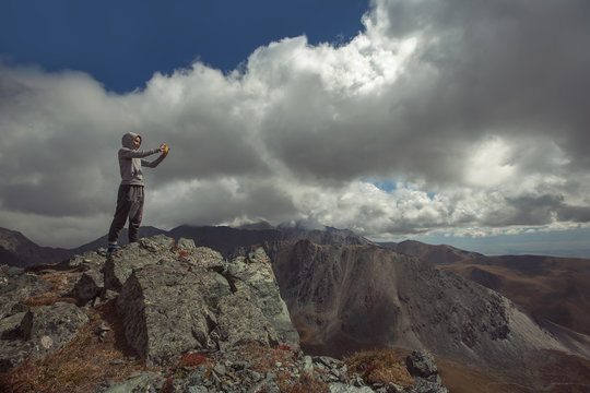 woman standing on mountain top and makes photo on  cell phone