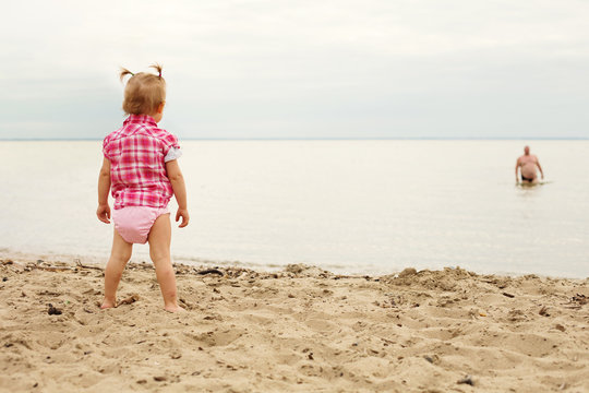 Little girl standing on the beach looking to fat man comes out to the shore