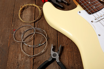 Electric guitar with pliers and cords on wooden background, close up