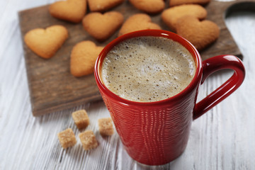Red cup of hot cacao and heart shaped cookies on wooden background