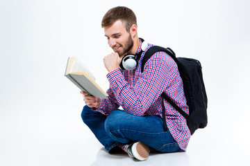 Cheerful handsome bearded man with backpack and headphones reading book