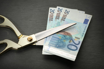 Golden scissors cut money on black background