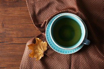 Cup of tea with autumn leaf on wooden table.