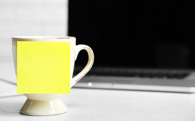 Yellow adhesive note on coffee cup, on laptop background