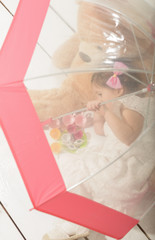 Expressive beautiful little girl having a tea party with her teddy bear, sitting under umbrela, indoor.