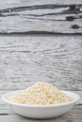 White sesame seed in white bowl over wooden background