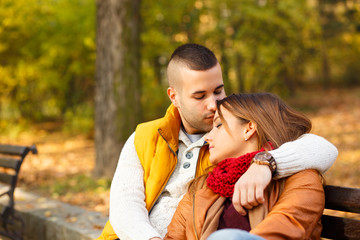 Young couple sitting on a park bench on a sunny autumn day and expressing tenderness