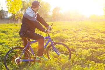 Obraz premium Young man cycling on a rural road through green spring meadow du