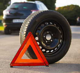 New tyre wheel and warning red triangle on road near broken auto