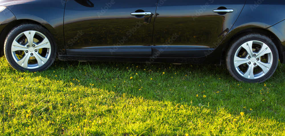 Wall mural black car without a trade brand on grass at sunset