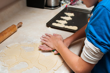 Fototapeta na wymiar hands of a child cutting christmast cookies out of rolled cookie dough