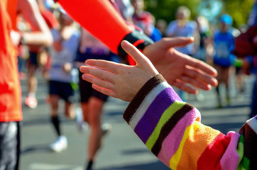 Marathon running race, support runners on road, child's hand giving highfive