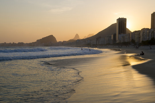 Golden sun setting behind a silhouette of the Rio de Janeiro skyline at the Leme end of Copacabana Beach