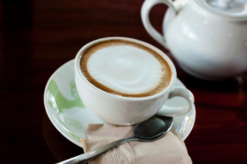 Cup of coffee with hot tea pot on wooden in over dark tone