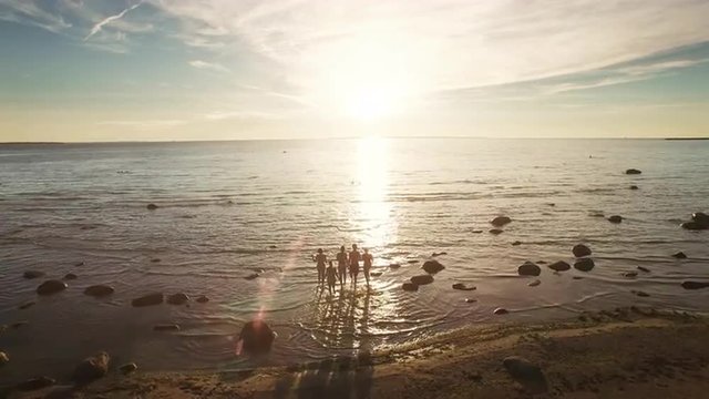 Aerial Drone Shot Of Group Of People Running Into Water At Sunset. 