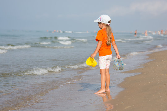 Girl standing on the beach with a bucket and slaps hands