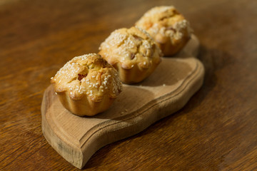 Three salty muffins with sausage, cheese and sesame on wood cut boarding.